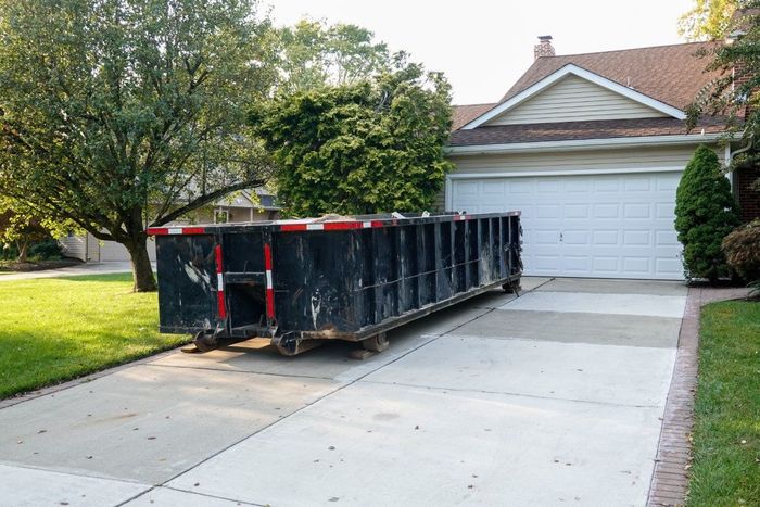 Black dumpster on a driveway in front of a house.