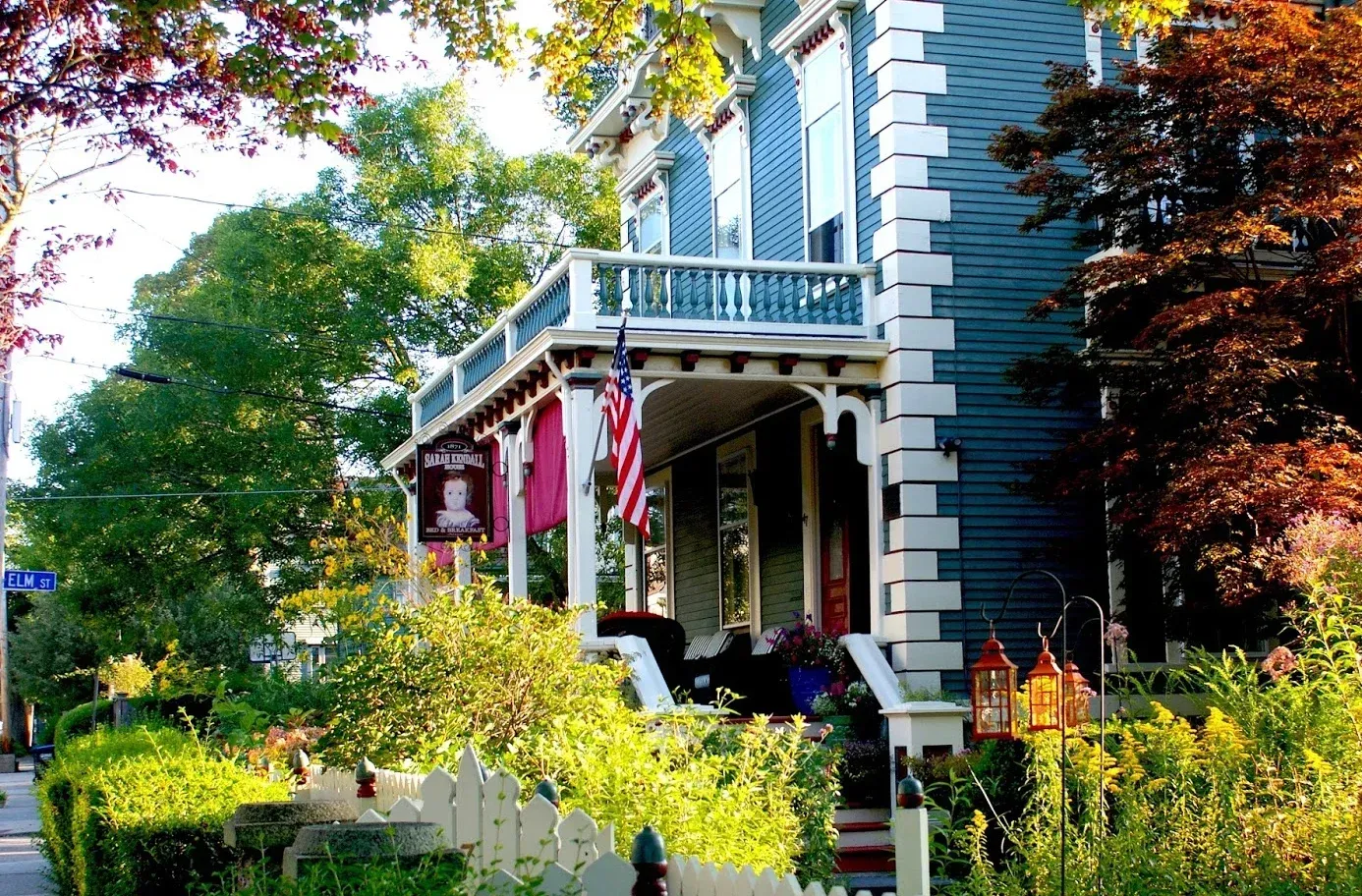 Victorian house with blue siding, white trim, and a sunlit garden in front