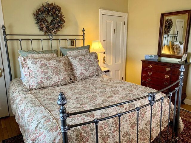 Floral bedspread on wrought-iron bed in a cozy bedroom with dresser, lamp, and mirror