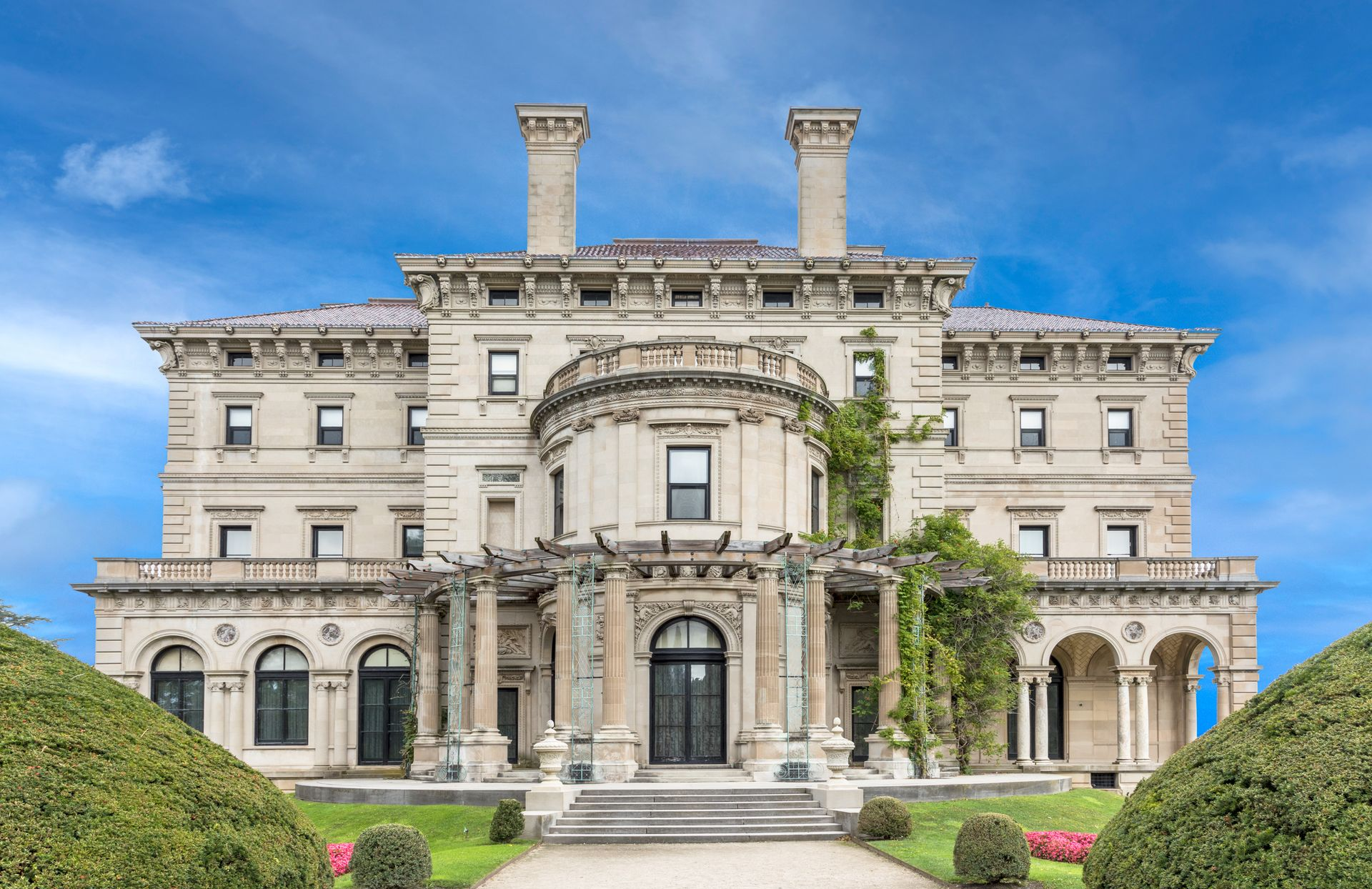 Grand historic mansion with arched entry, stone façade, and manicured green lawn under a blue sky