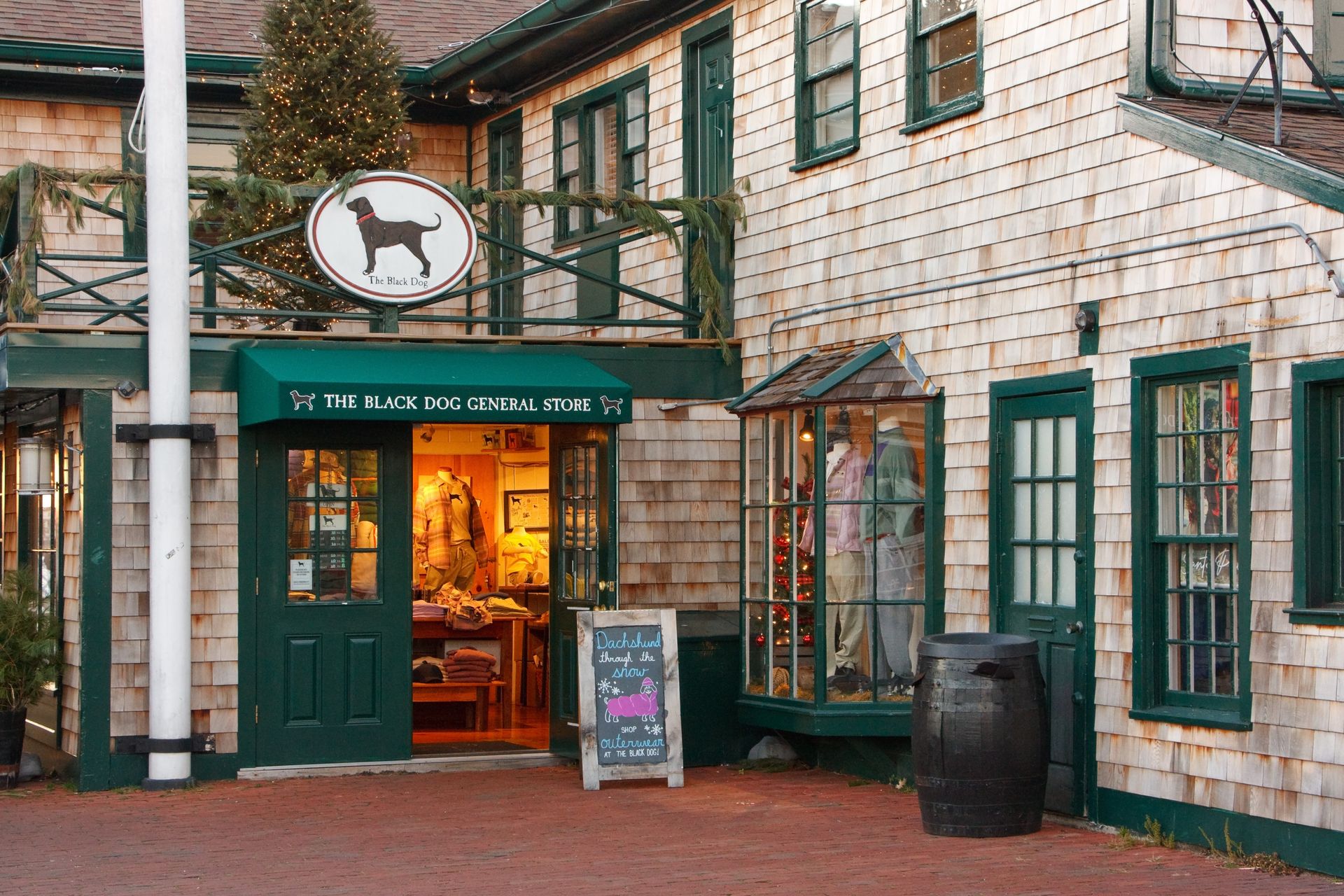Brick storefront with green trim and a dog sign above the entrance, warmly lit from inside.