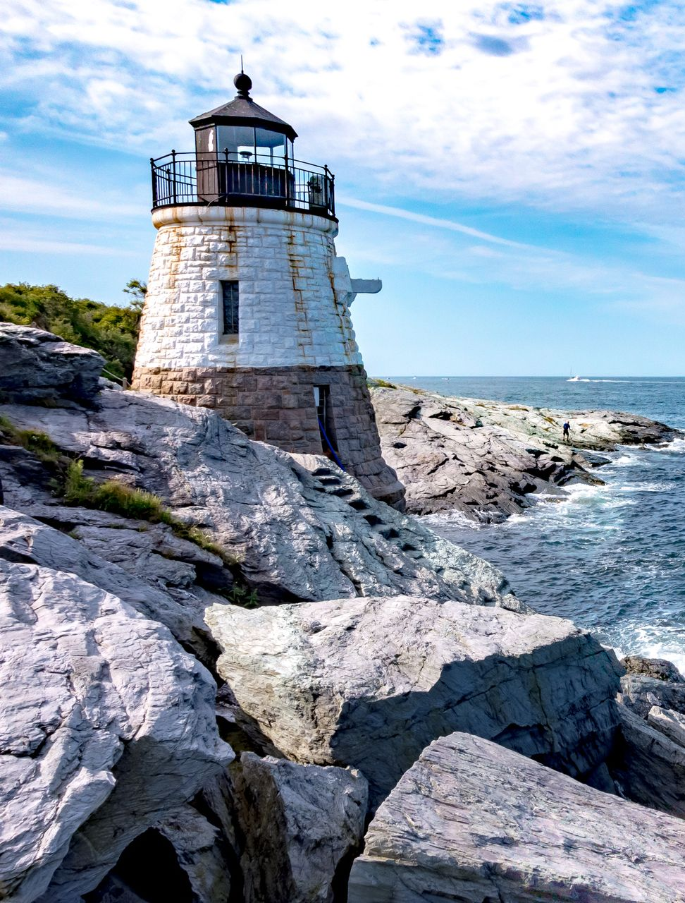 Stone lighthouse on rocky coast beside the ocean under a bright blue sky