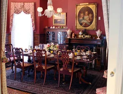 Elegant dining room with red walls, long table set with china, and ornate paintings above a fireplace