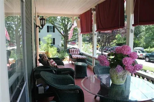 Porch seating area with wicker chairs, glass table, and pink flowers overlooking a garden