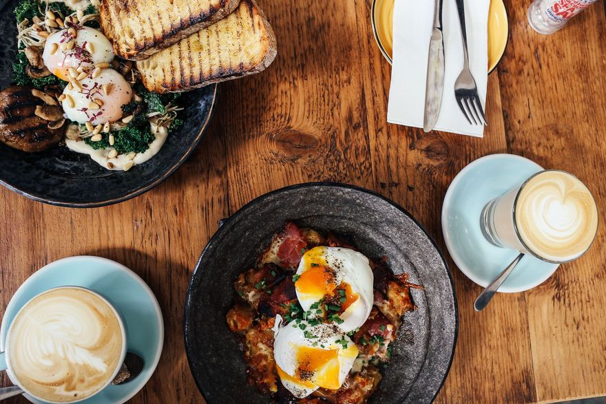Brunch table with toast, eggs, coffee, and plated dishes on a wooden surface