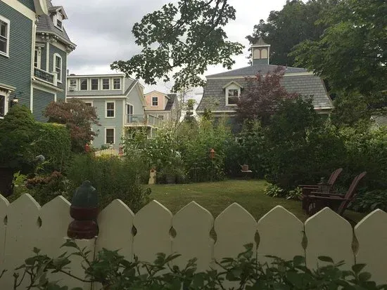 Garden view with white picket fence, green lawn, shrubs, and pastel houses in the background