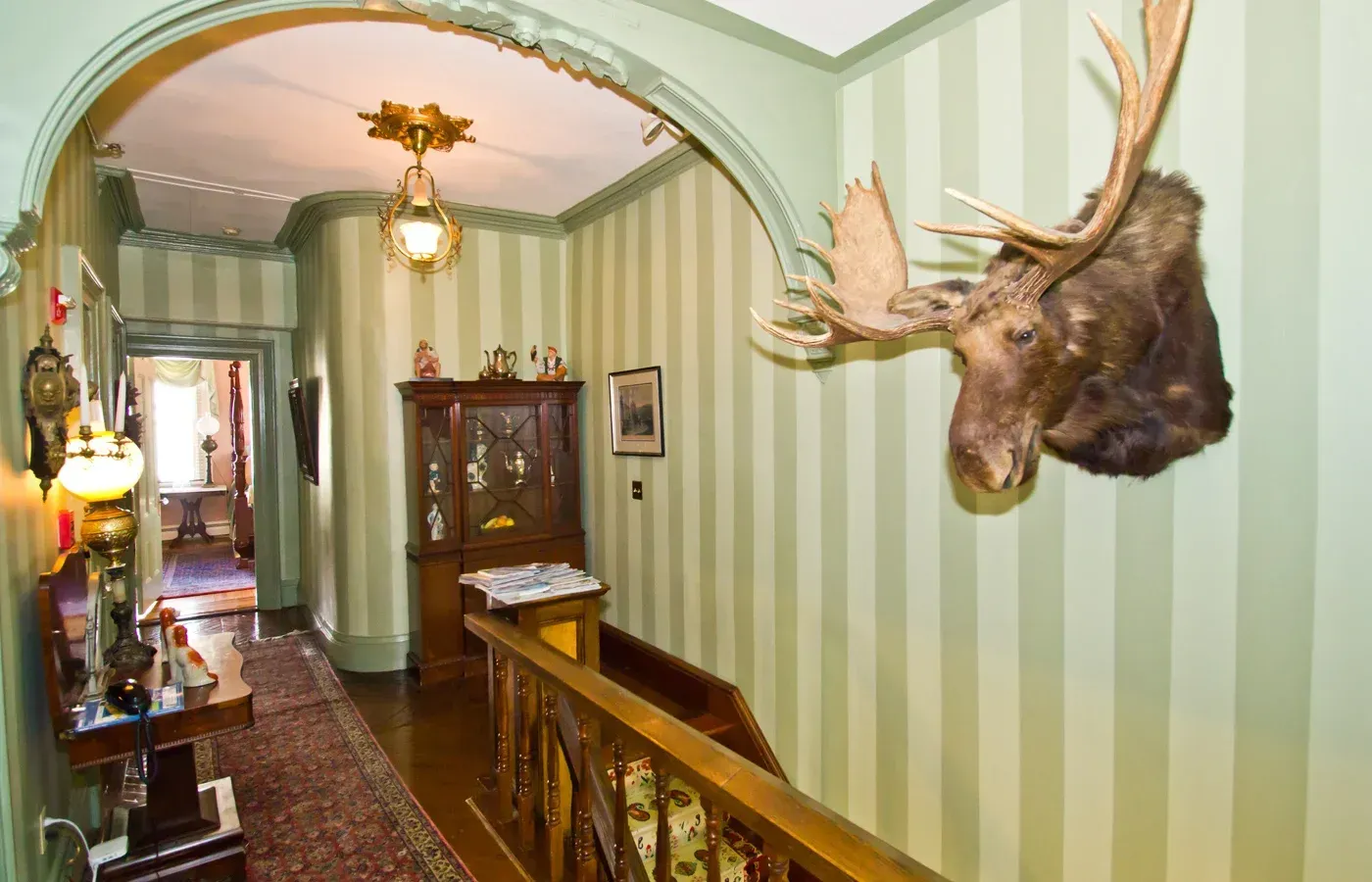 Hallway with green striped walls, mounted moose head, and antique furniture under an archway