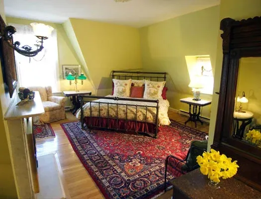 Cozy bedroom with a dark wood bed, red patterned rug, yellow walls, and bedside lamps