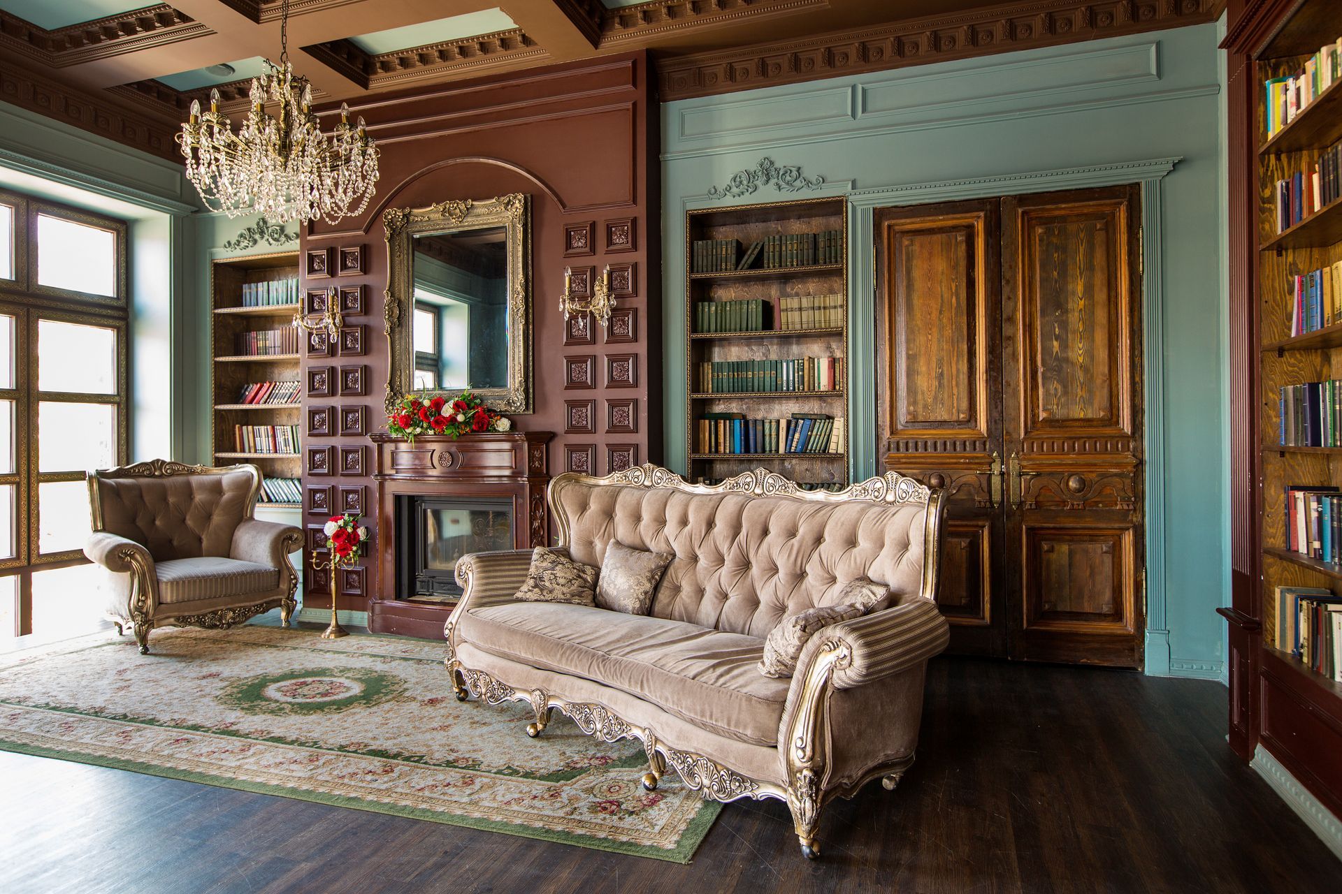 Elegant living room with tufted sofa, armchair, bookshelves, chandelier, and wood-paneled cabinets