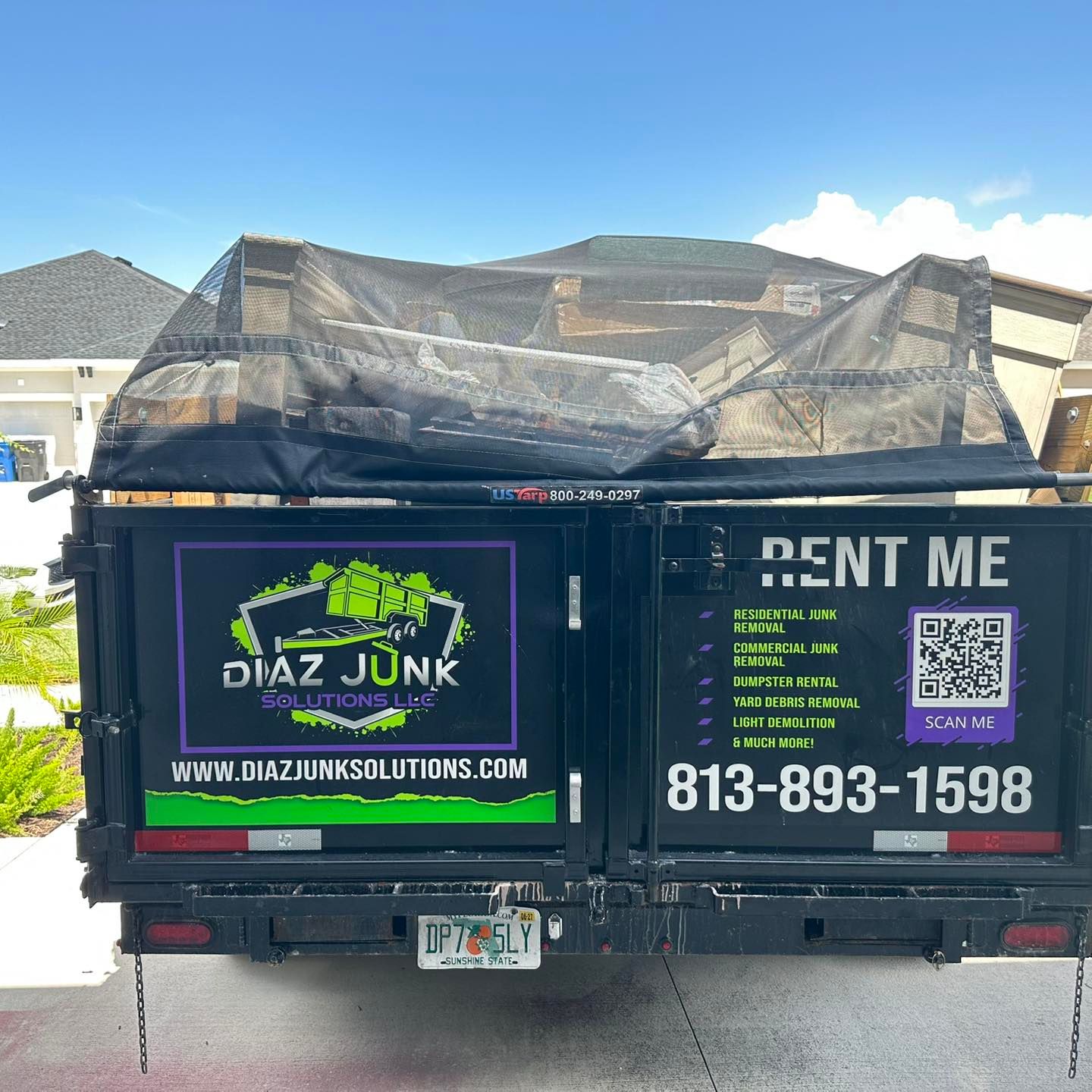 A black Diaz Junk Solutions truck with a full bed, parked outside a house.