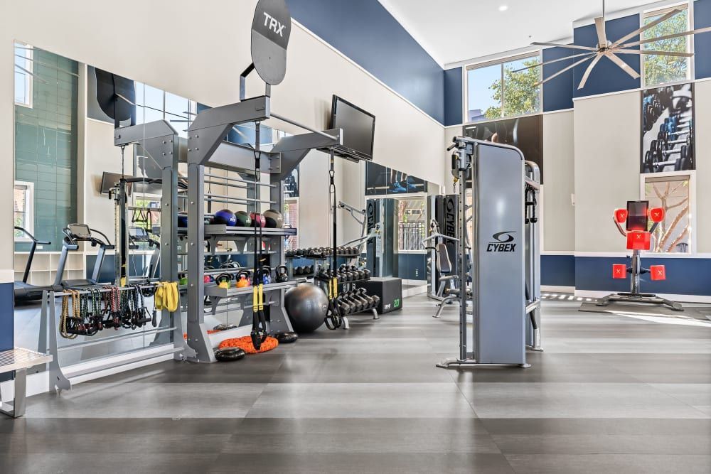 Modern gym interior with a variety of exercise equipment, including weight machines, TRX bands, free weights, exercise balls, and treadmills, under bright lighting and a high ceiling at Marq Inverness in Englewood, CO.