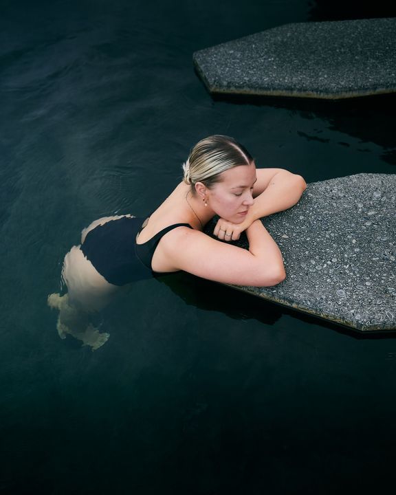 Woman resting in dark water beside a speckled stone ledge