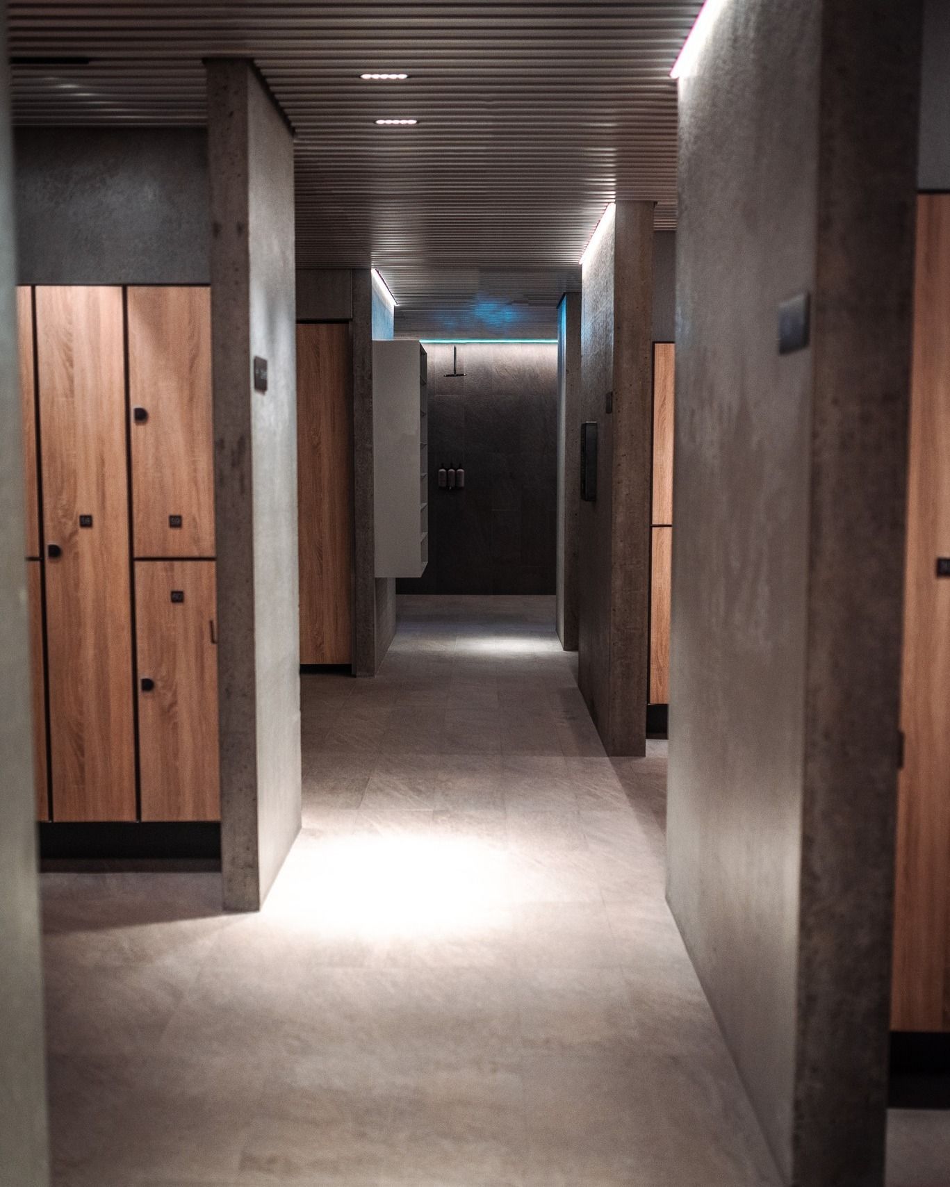Modern hallway with wood lockers, concrete walls, and a lit doorway at the end