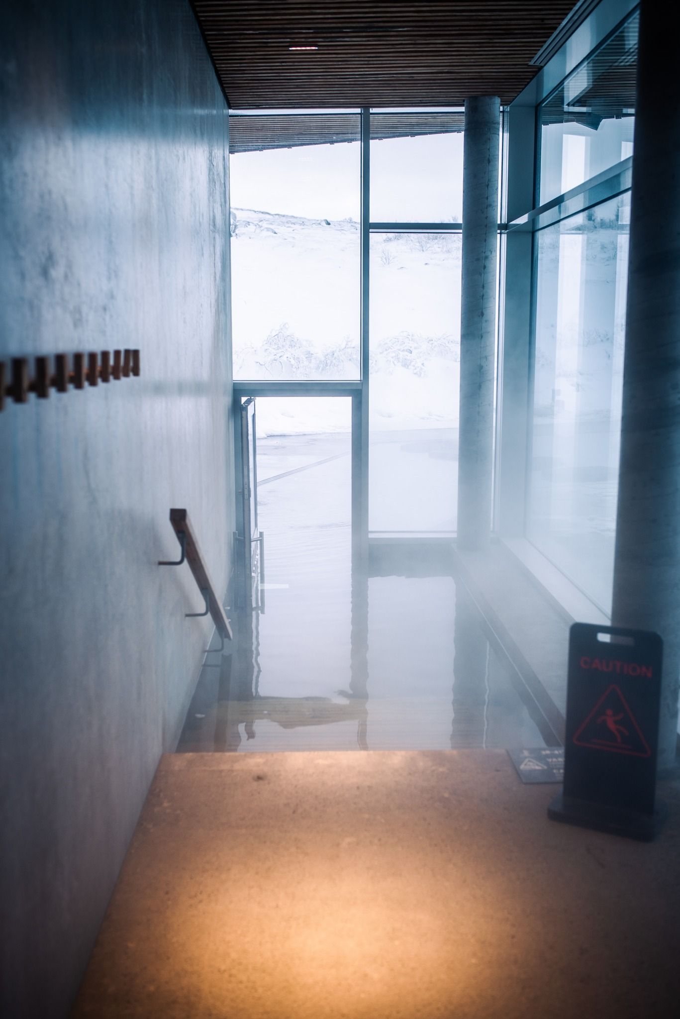 Modern hallway with glass doors, frosted panels, and warm floor lighting amid cool blue walls