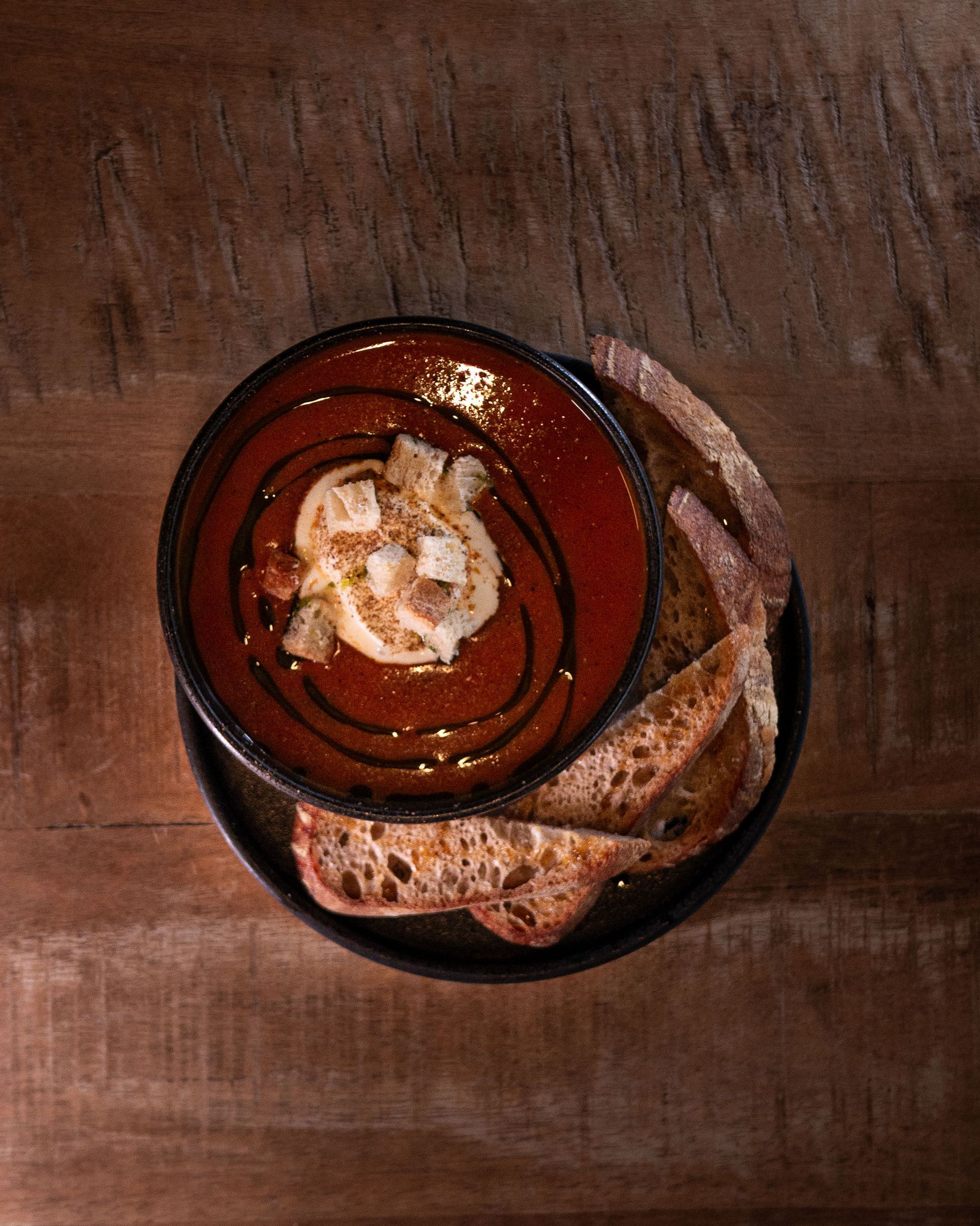 Top-down view of a bowl with soup or stew and bread on a dark wooden table