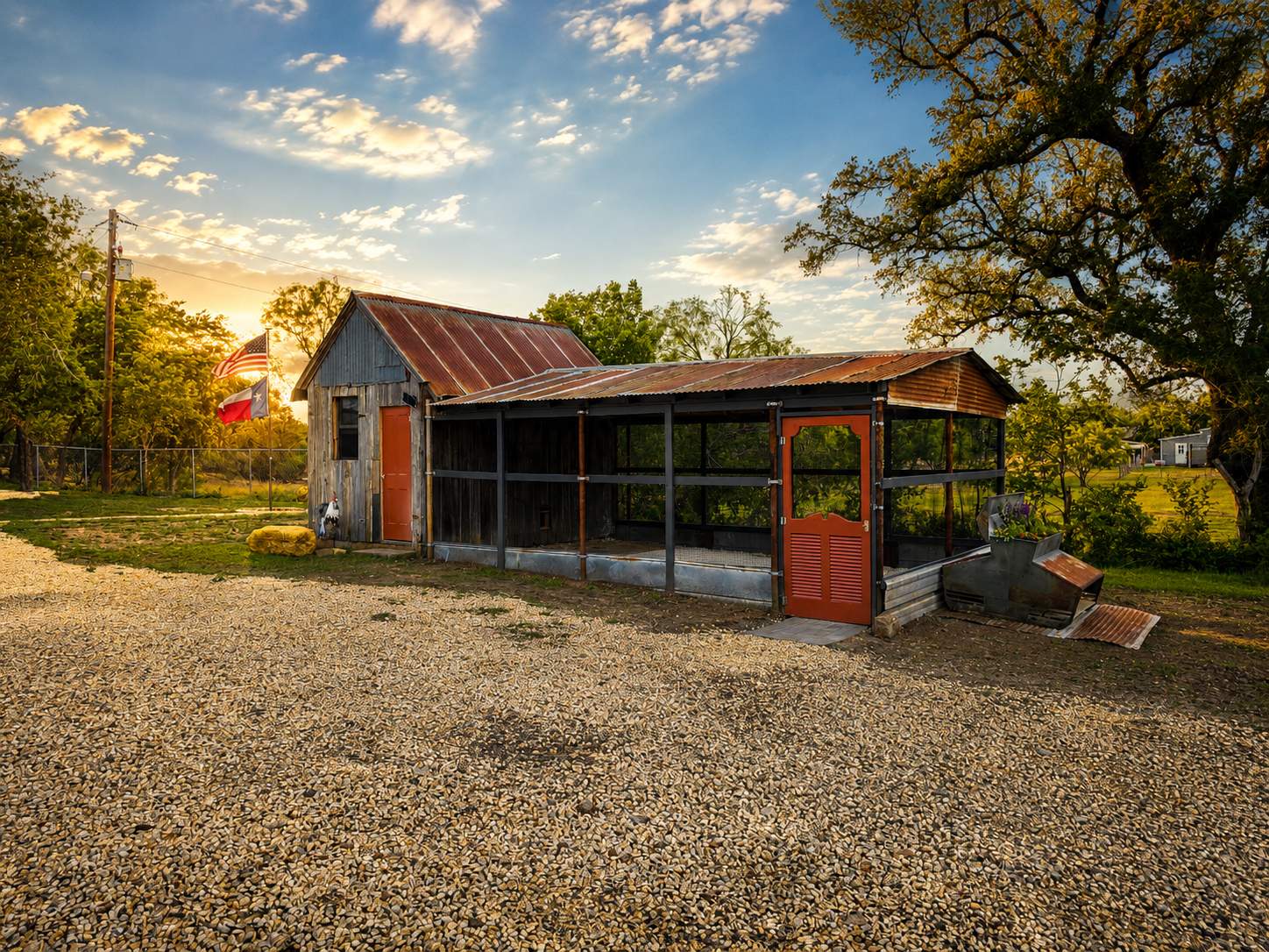 Rustic red-roofed shed with screened porch in a gravel yard at sunset, surrounded by trees