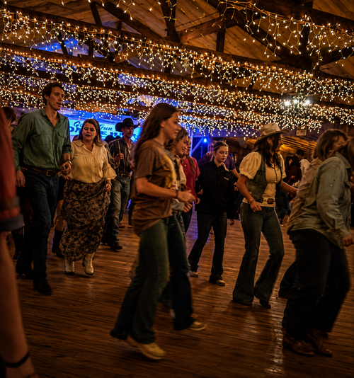 People dancing on a wooden floor under warm string lights in a festive indoor venue