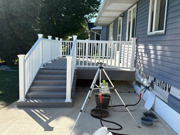 Front porch stairs and deck under construction, with white railings and tools set up on the ground.
