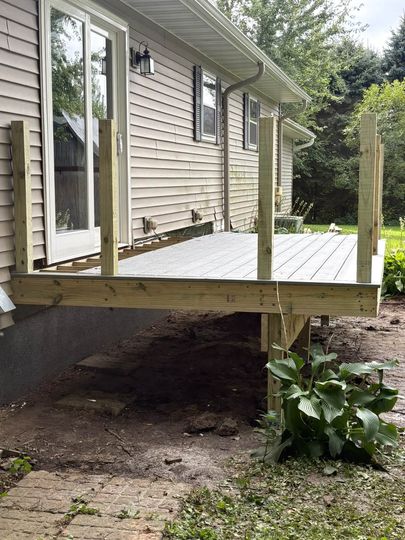 Raised wooden deck under construction beside a house, with exposed posts and unfinished framing.