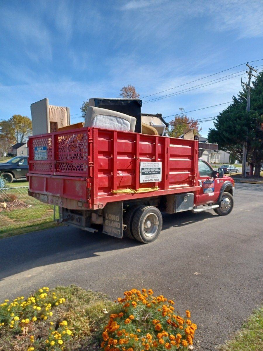 Red dump truck loaded with debris parked on a residential street beside flowers and houses