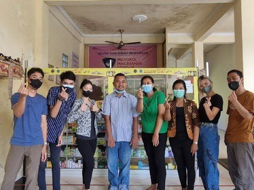 Sekelompok orang berpose di dekat etalase dengan mengacungkan jempol dan mengenakan masker wajah.