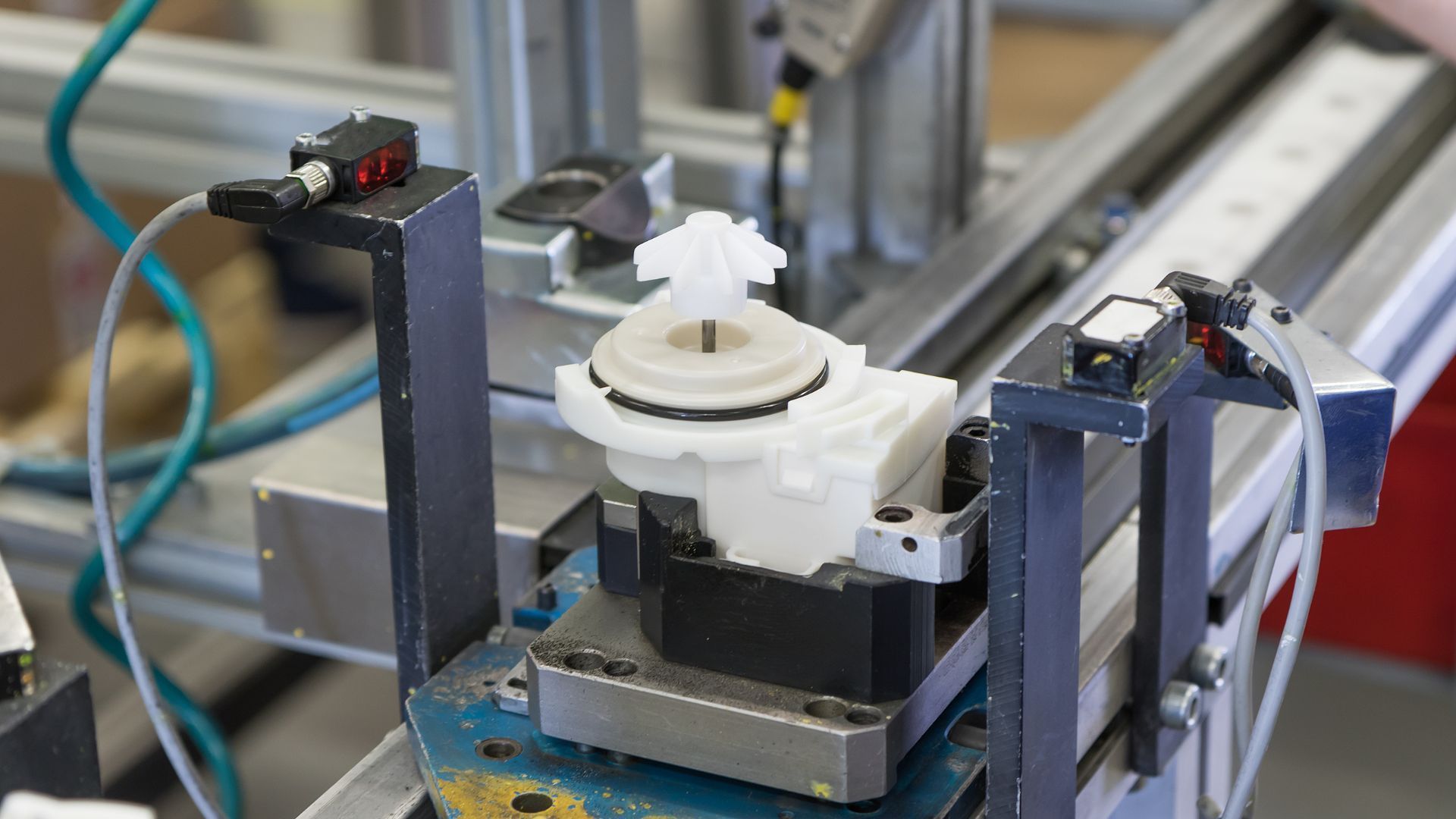 Industrial machine with a white rotating component clamped between dark metal supports on a factory bench
