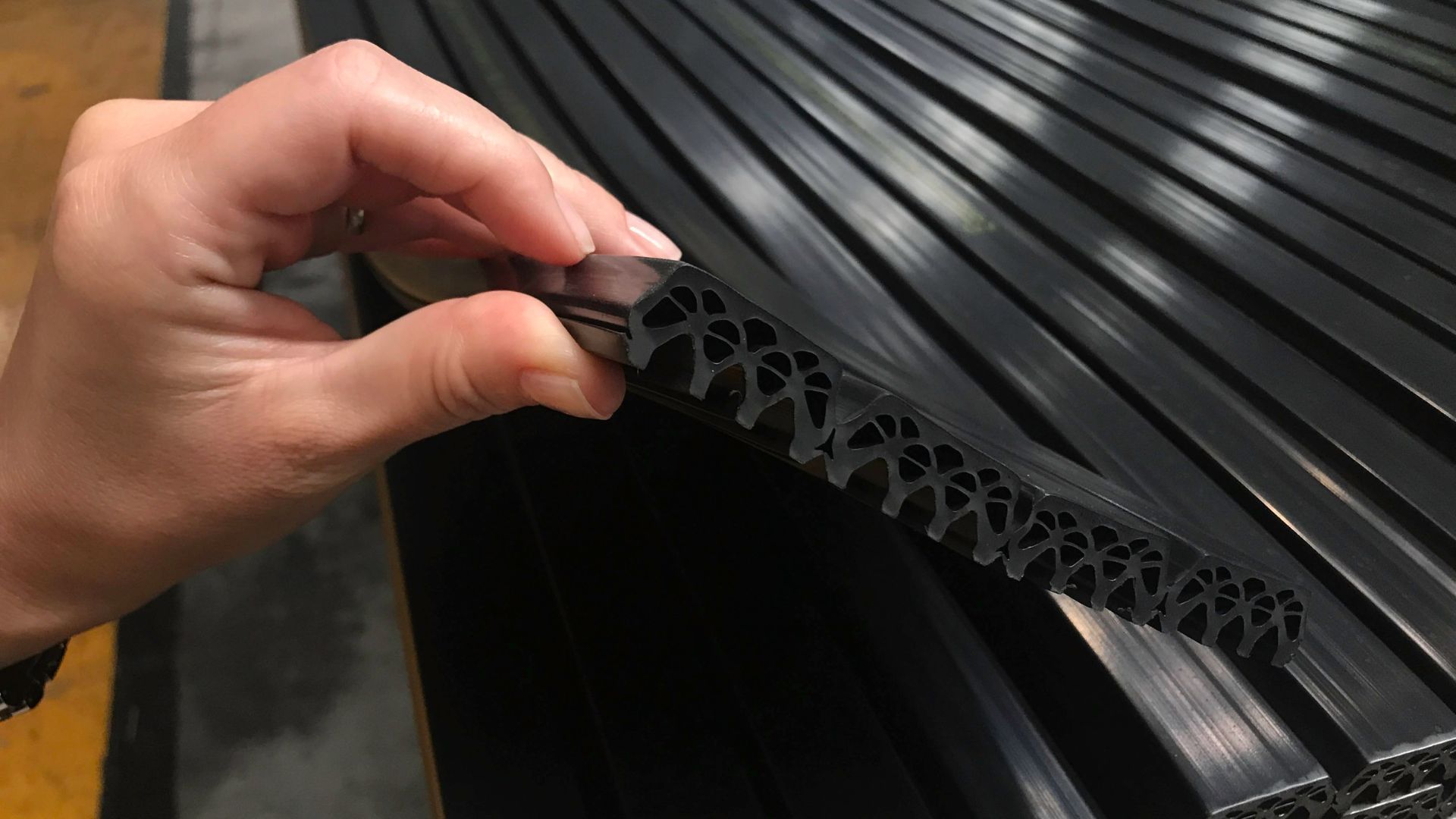 Hand holding a black flexible rubber strip over stacked black corrugated panels