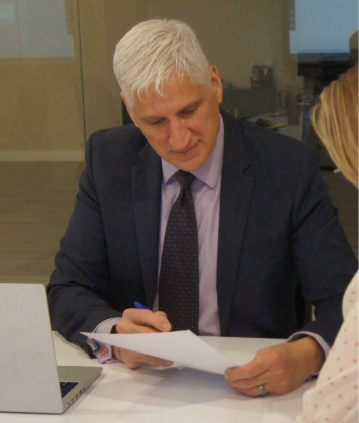 Three people reviewing documents at a table in a bright office meeting room.