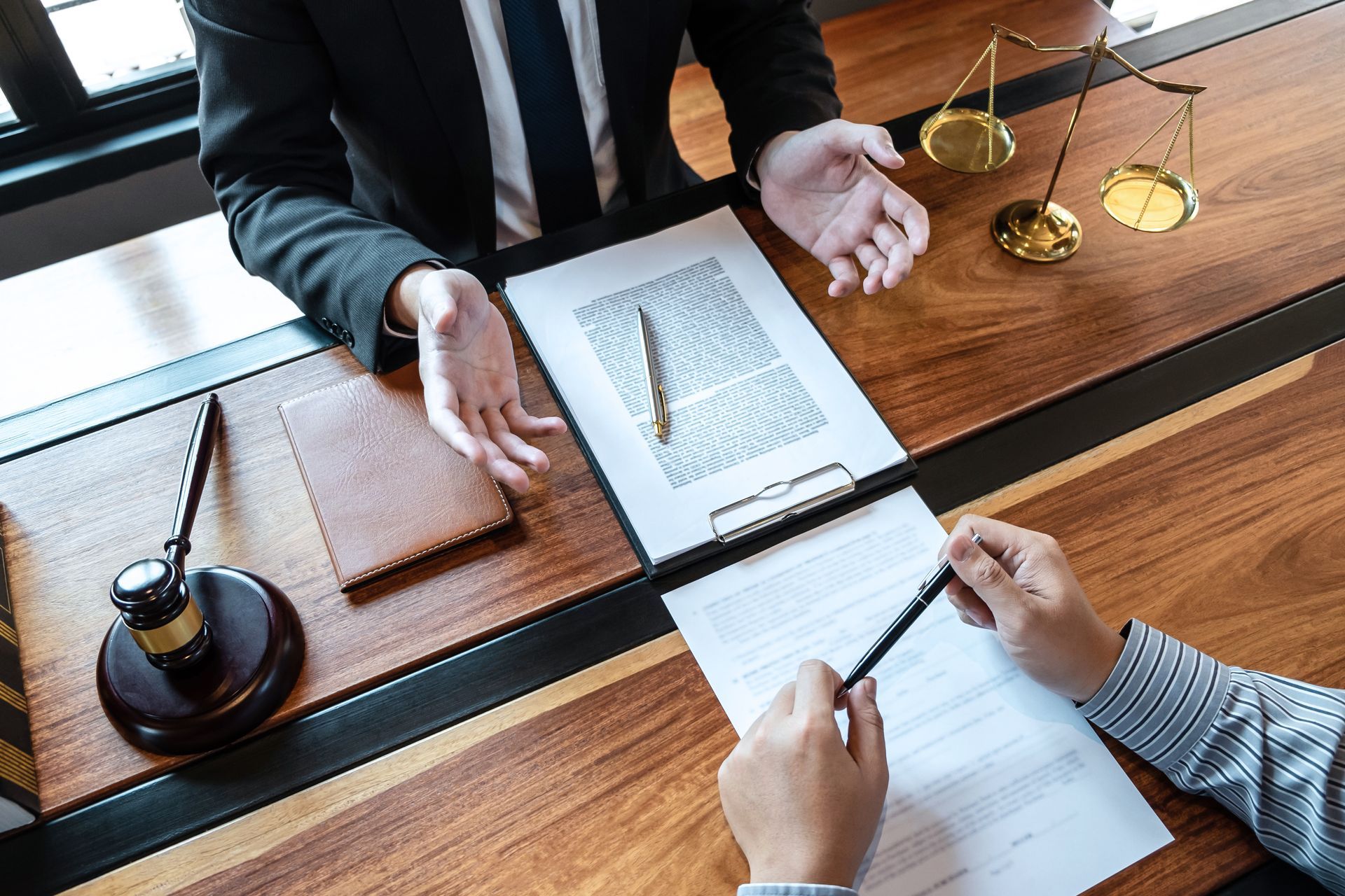 Two people reviewing documents and writing notes at a wooden meeting table with a gavel and scales.