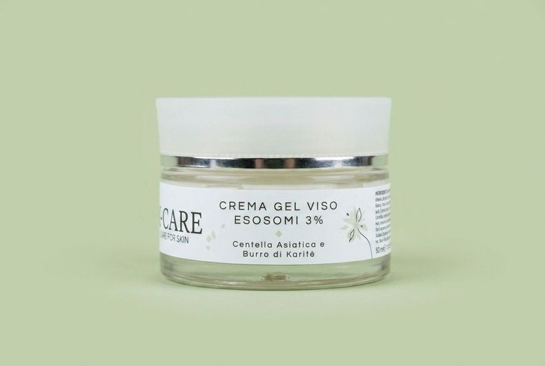 Vasetto bianco per crema per la cura della pelle con coperchio argentato su sfondo verde chiaro.
