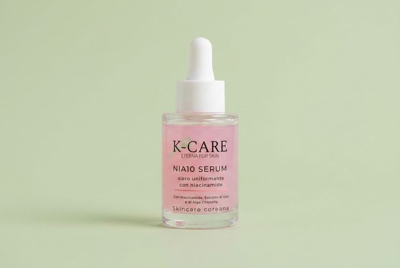 Flacone rosa di siero per capelli K-CARE con contagocce su sfondo verde chiaro.
