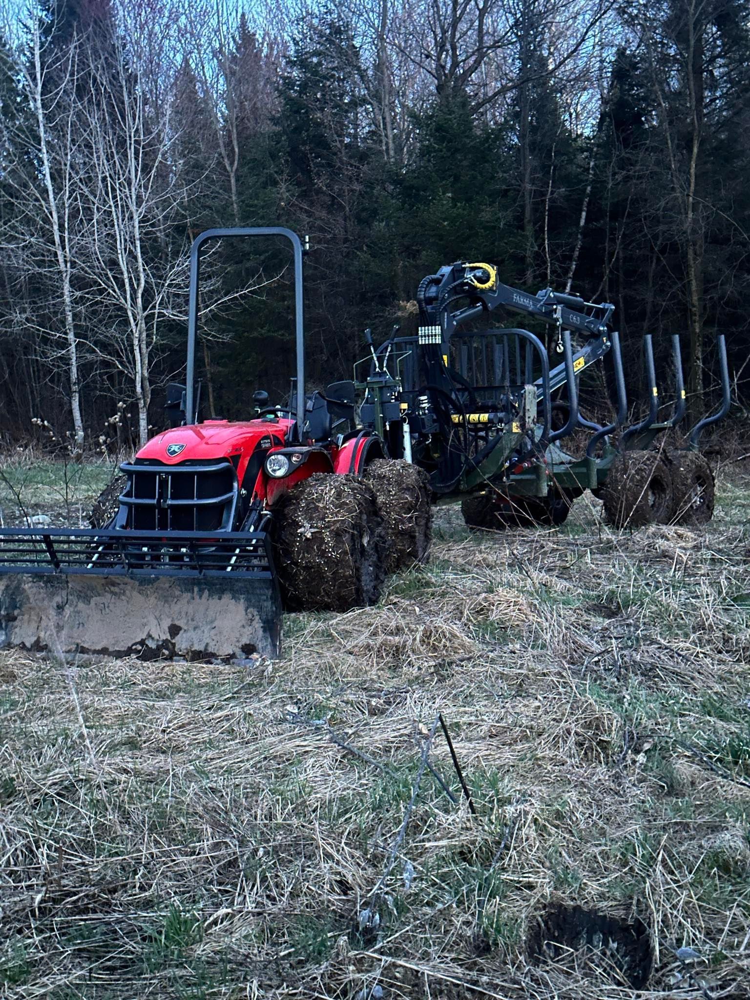 Un tracteur rouge traverse un champ avec des arbres en arrière-plan.