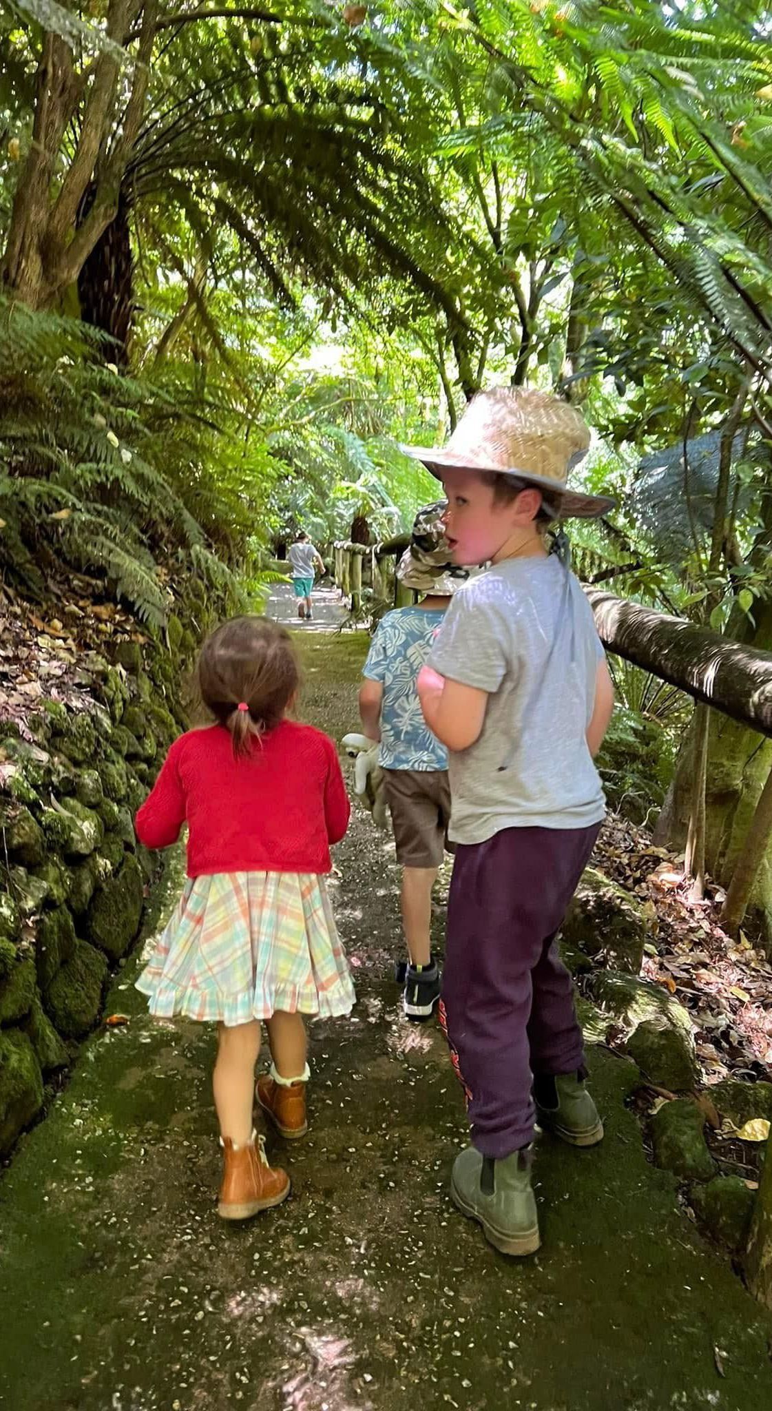 A boy and a girl are walking down a path in the woods.
