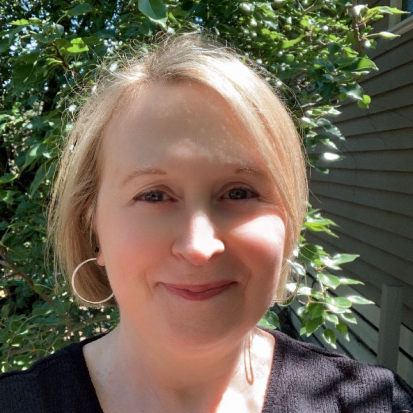 A woman with blonde hair and hoop earrings is smiling for the camera