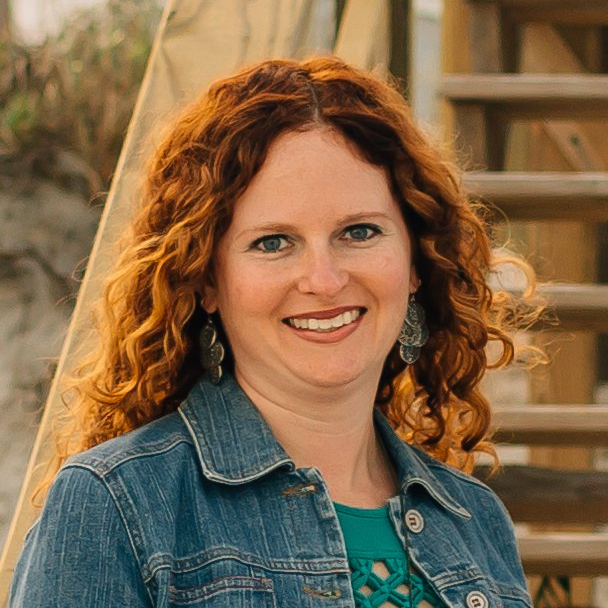 A woman with red hair is wearing a denim jacket and smiling