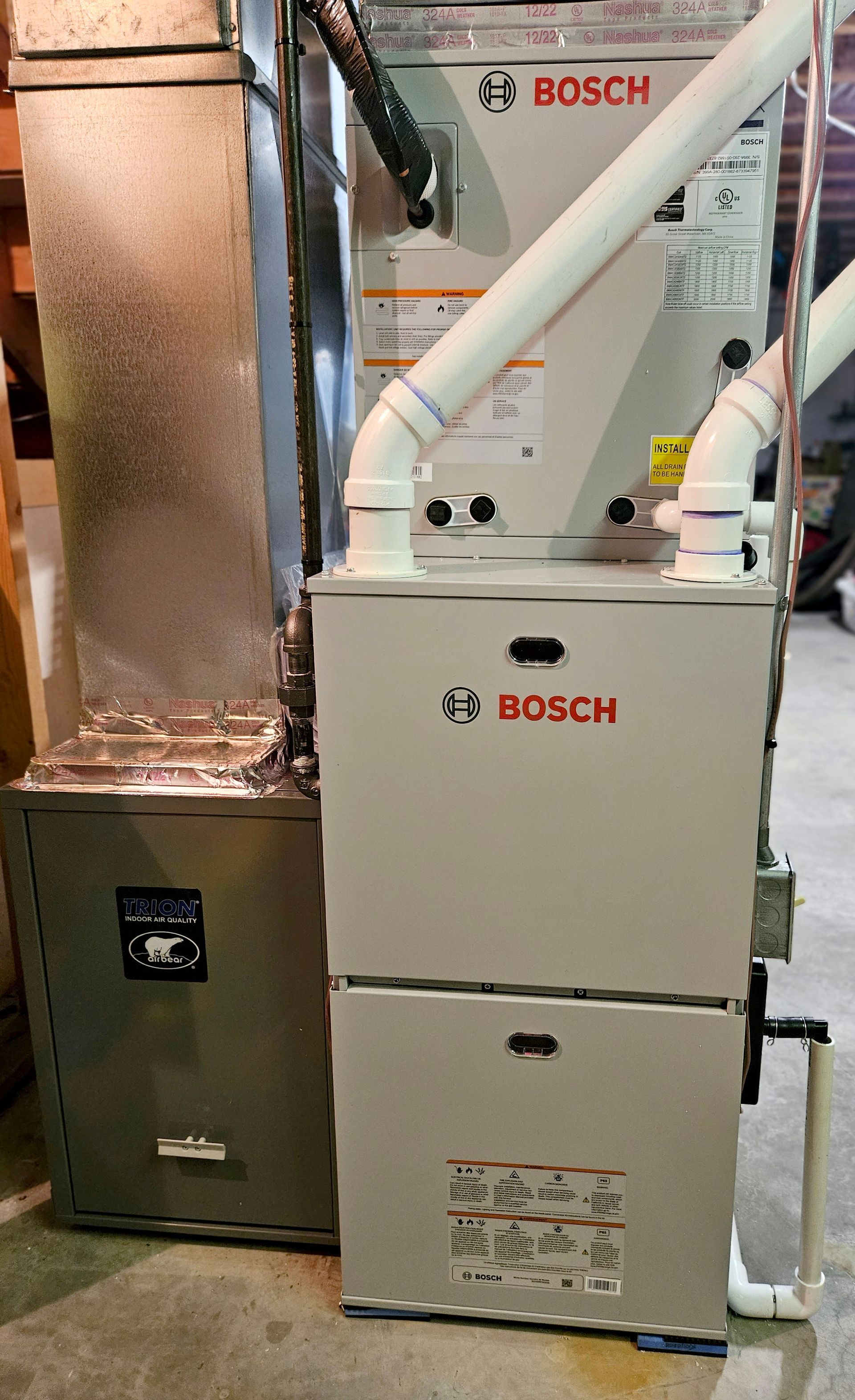 A bosch air conditioner is sitting next to a furnace in a basement.