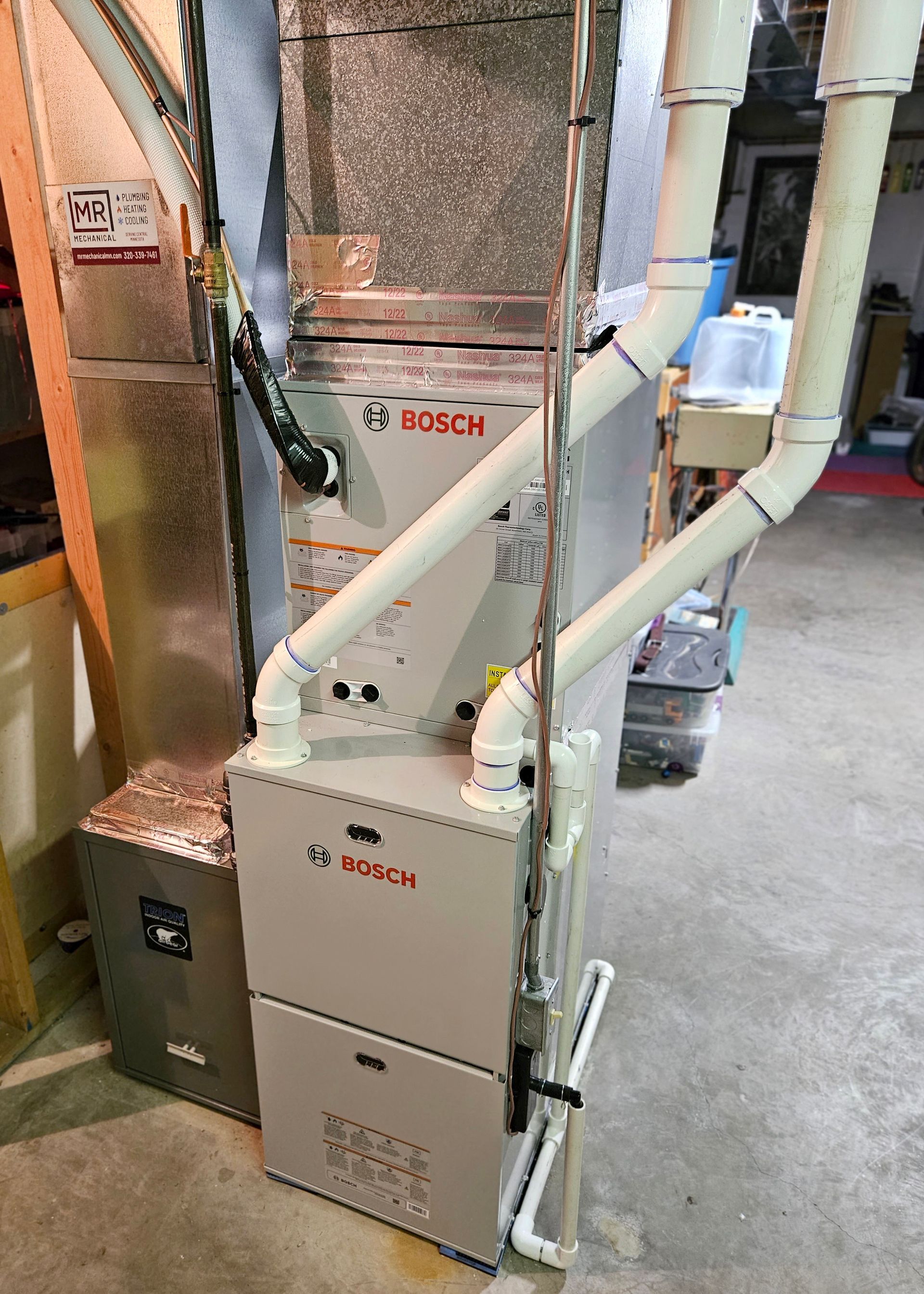 A bosch furnace is sitting in a basement next to a duct.