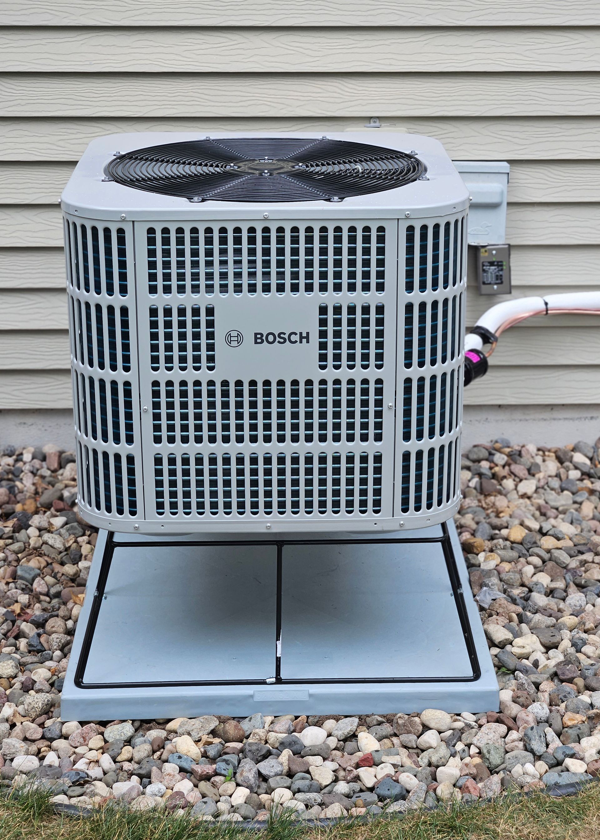 A bosch air conditioner is sitting on top of a pile of rocks next to a house.