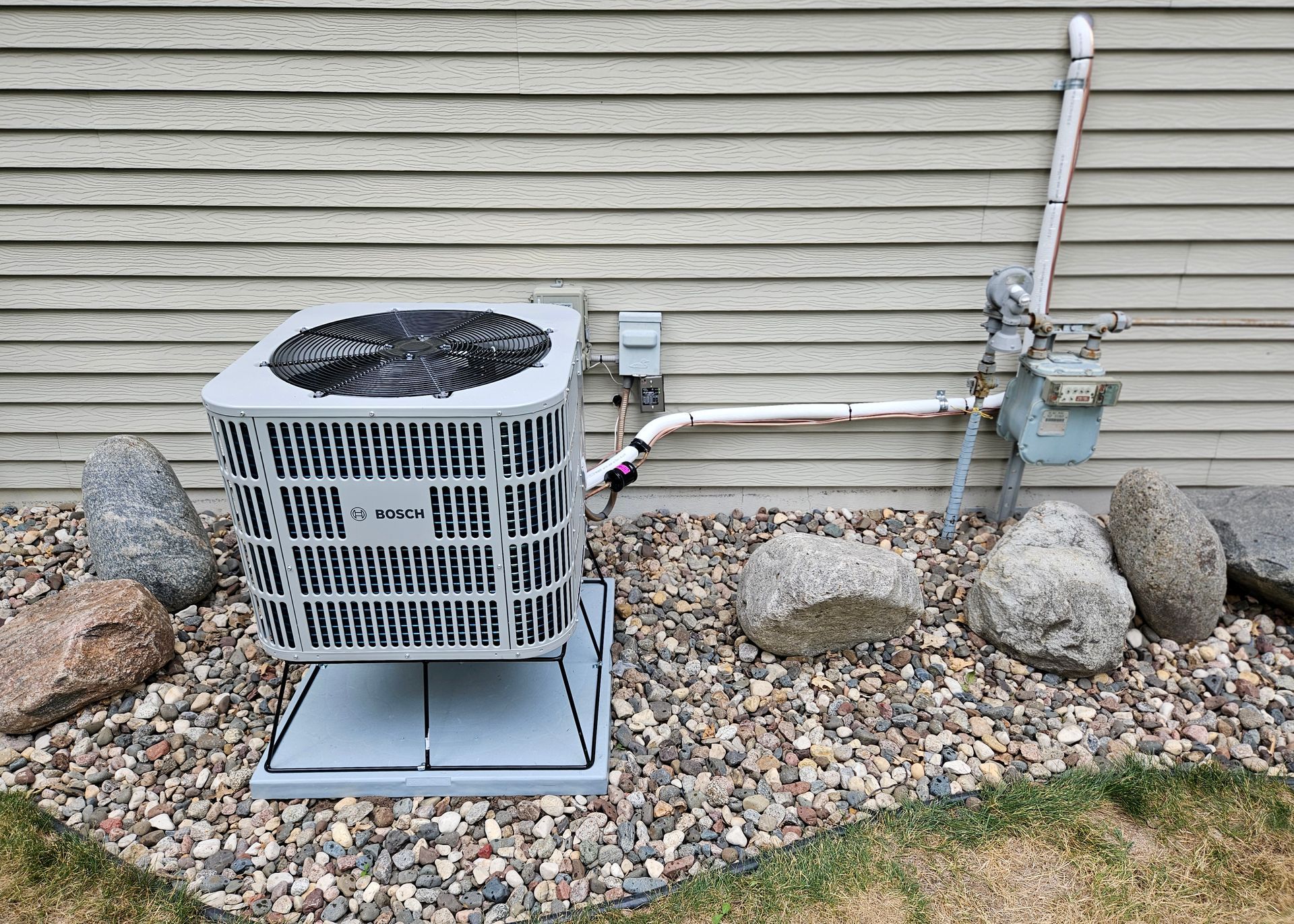 An air conditioner is sitting on top of a pile of rocks next to a house.