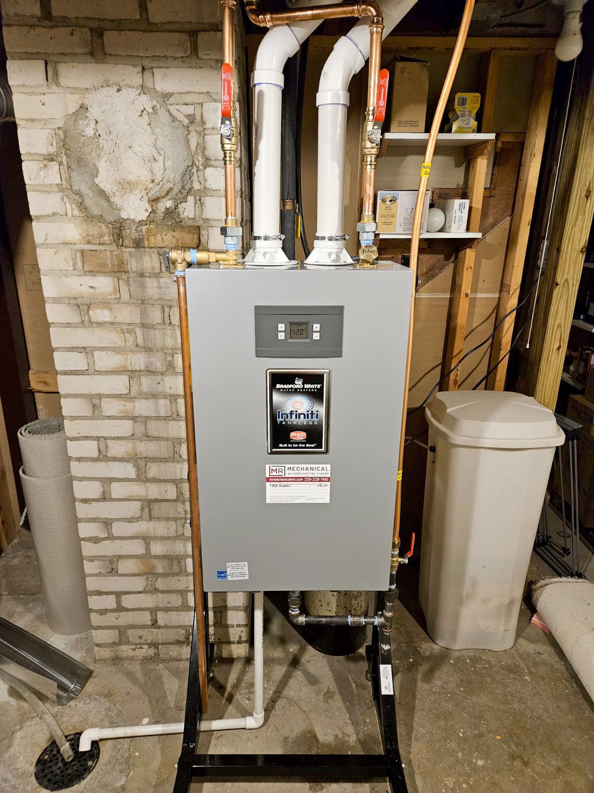 A boiler is sitting in a basement next to a brick wall.