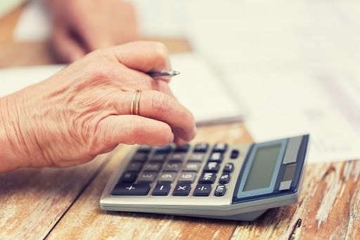 A person is using a calculator on a wooden table.