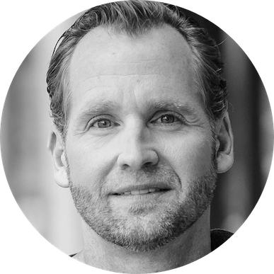 A man with a beard is smiling in a black and white photo.