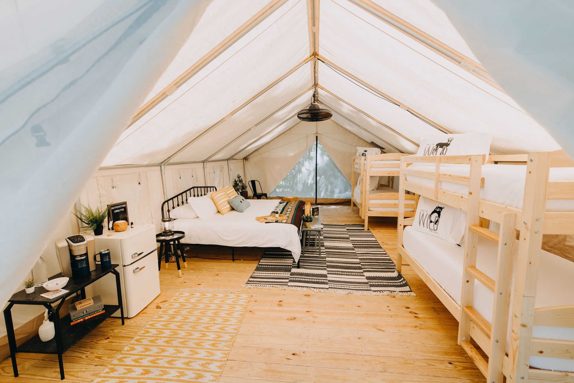 Inside of a large tent: beds, rug, small fridge, coffee maker. Wooden floor and walls, natural light.