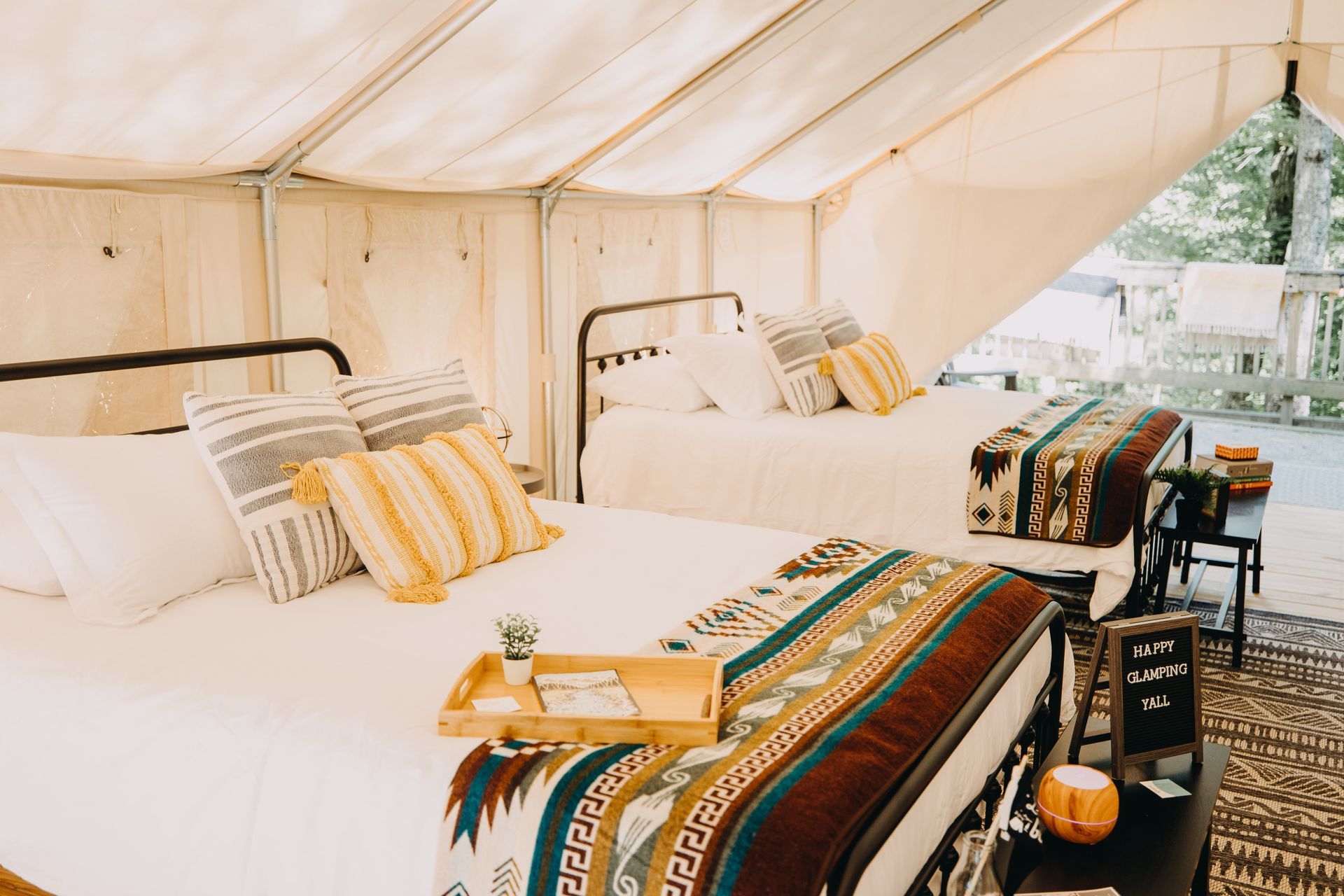 Two beds inside a tent, with decorative pillows, blankets, and a small table.