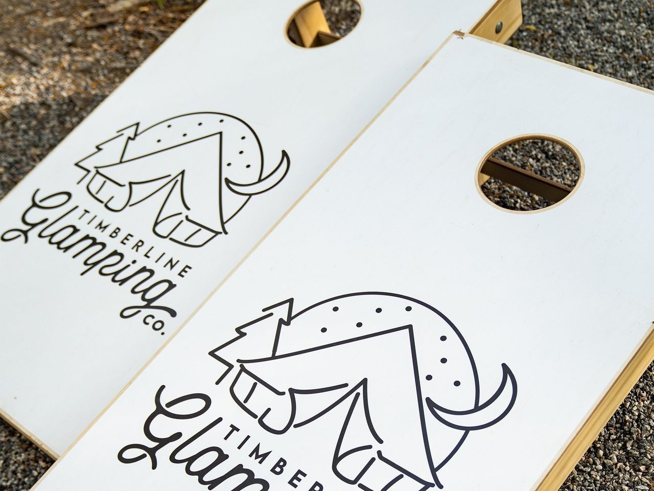 Two white cornhole boards with a black Timberline Glamping Co. logo.