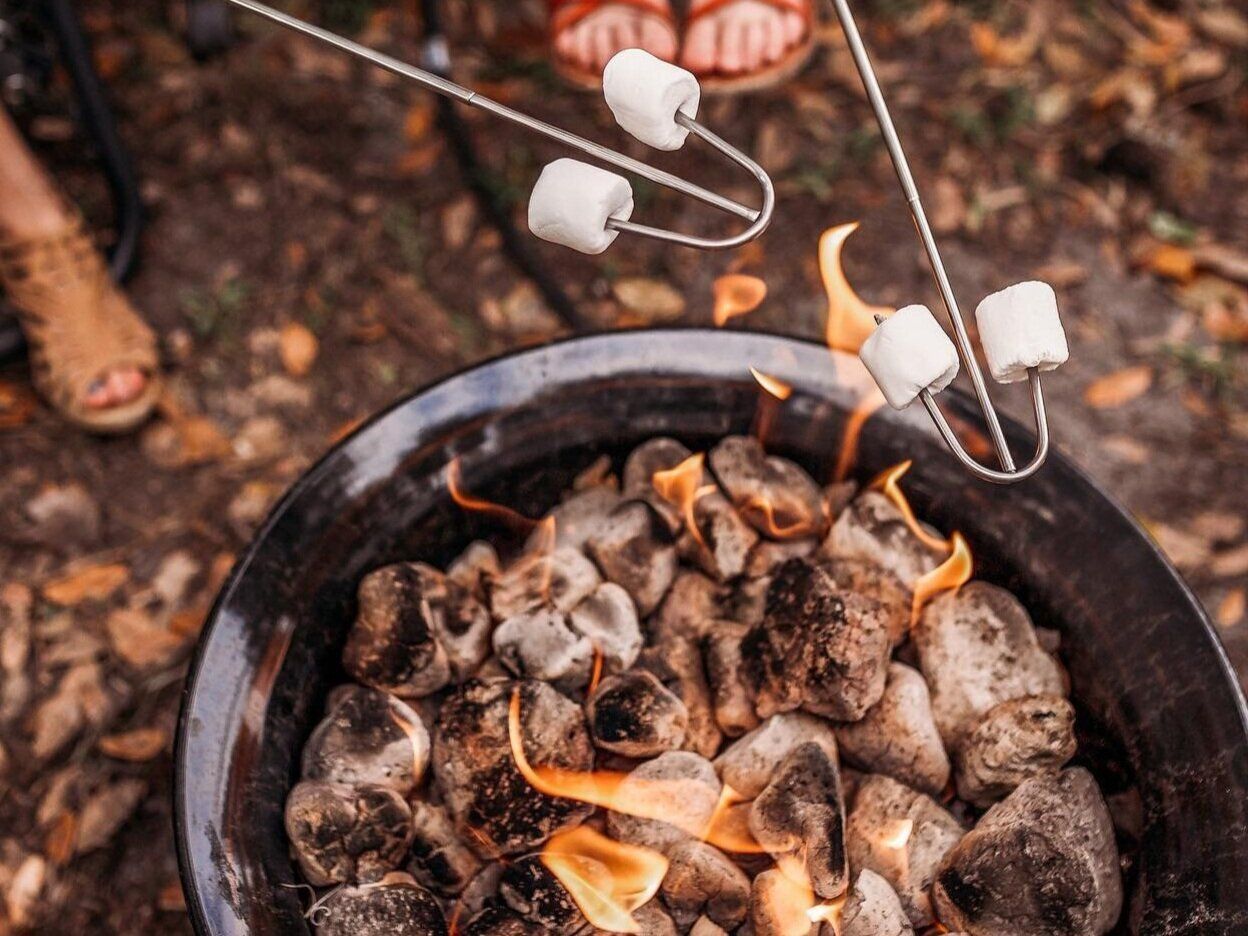 Marshmallows roasting over a charcoal fire pit with people nearby.