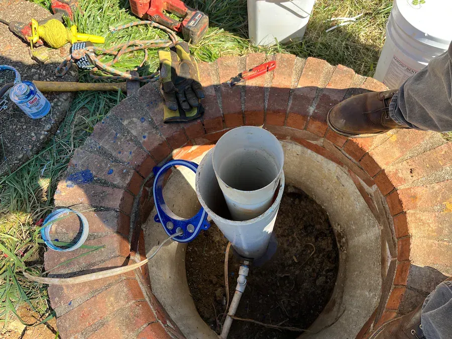 A man is standing in a hole with pipes in it.