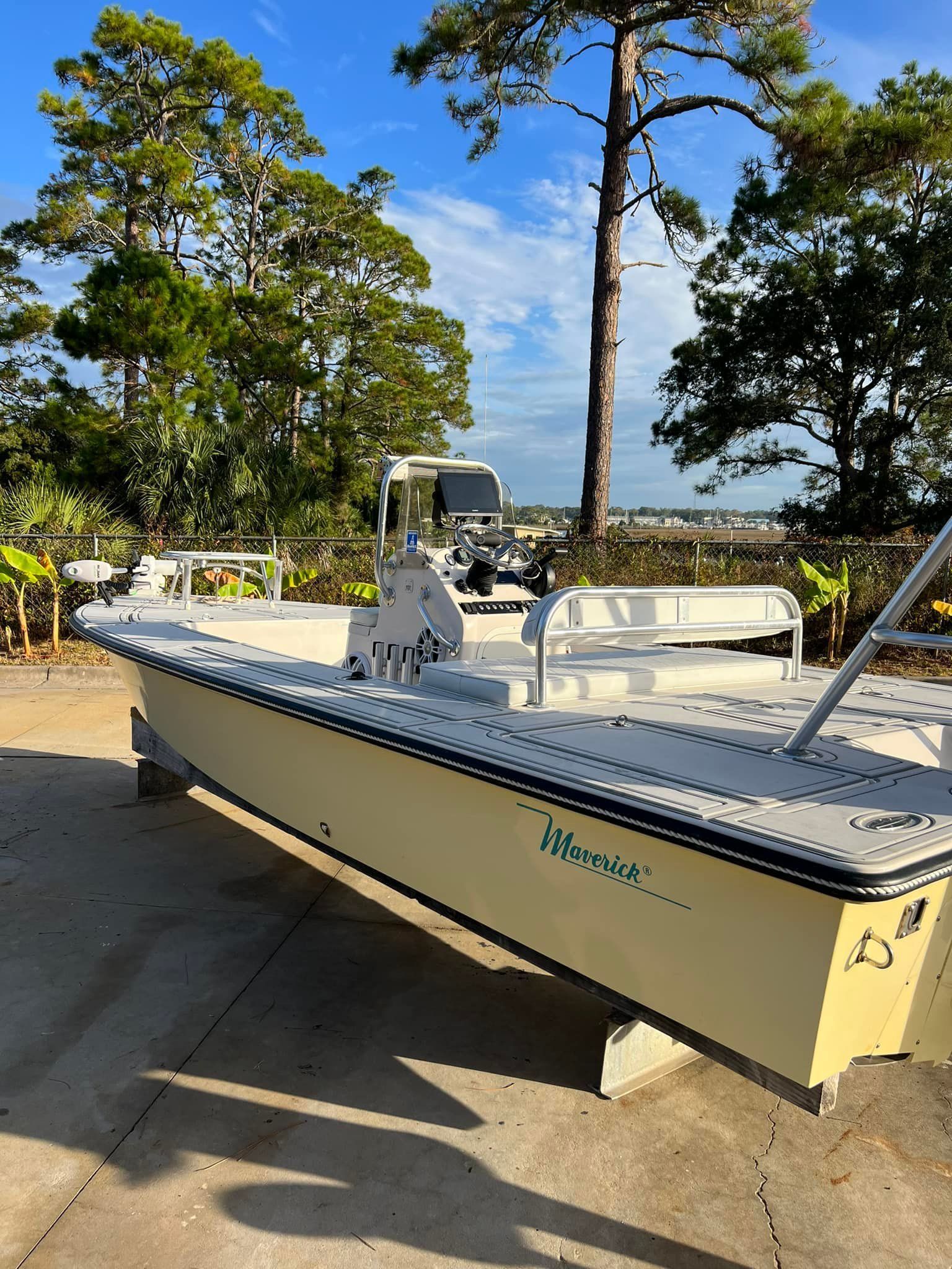 A white boat is parked on the side of the road in front of trees.