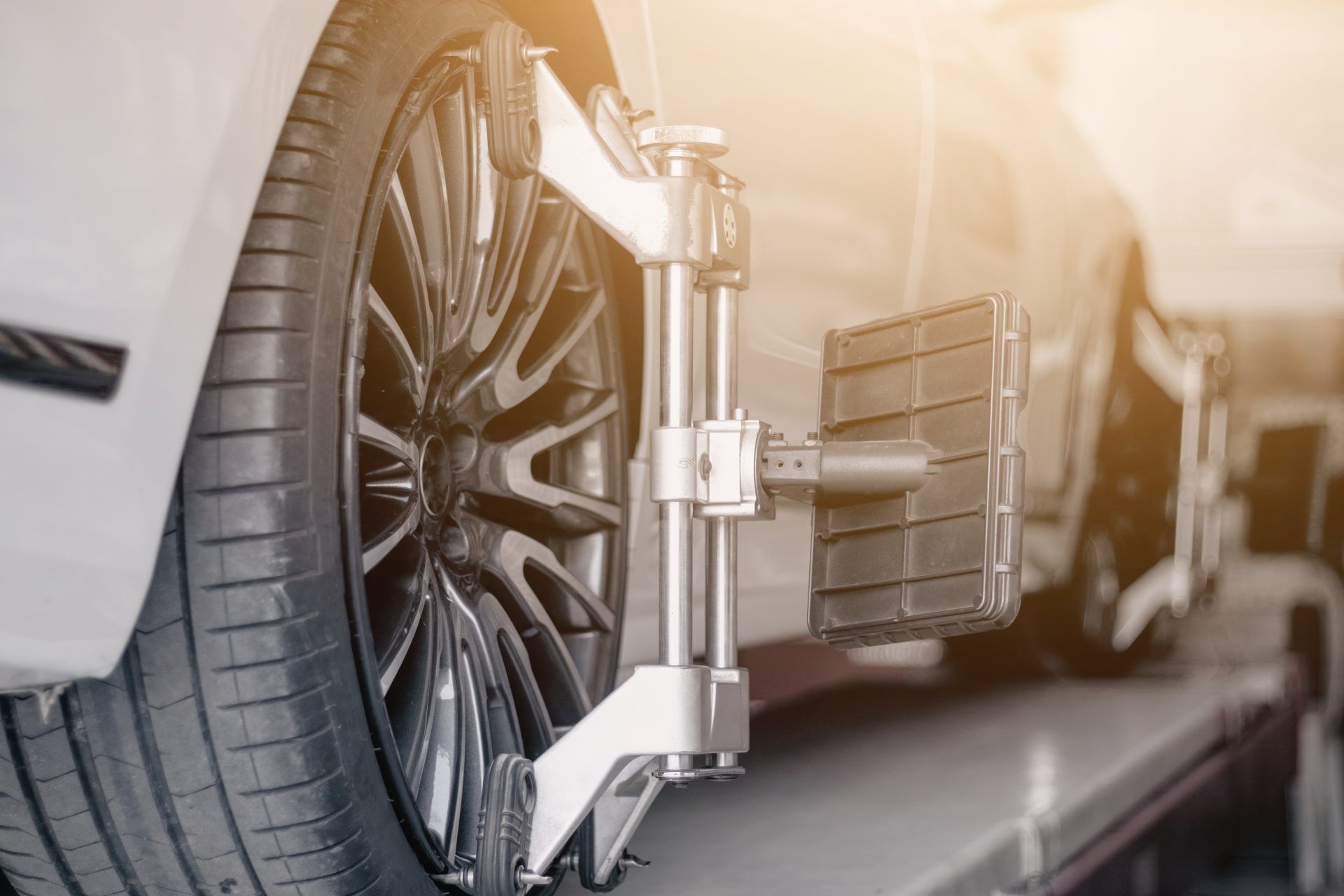 Car wheel on a lift undergoing alignment check with attached measuring device.