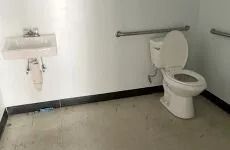 Sparse public restroom with toilet and wall-mounted sink against white walls.